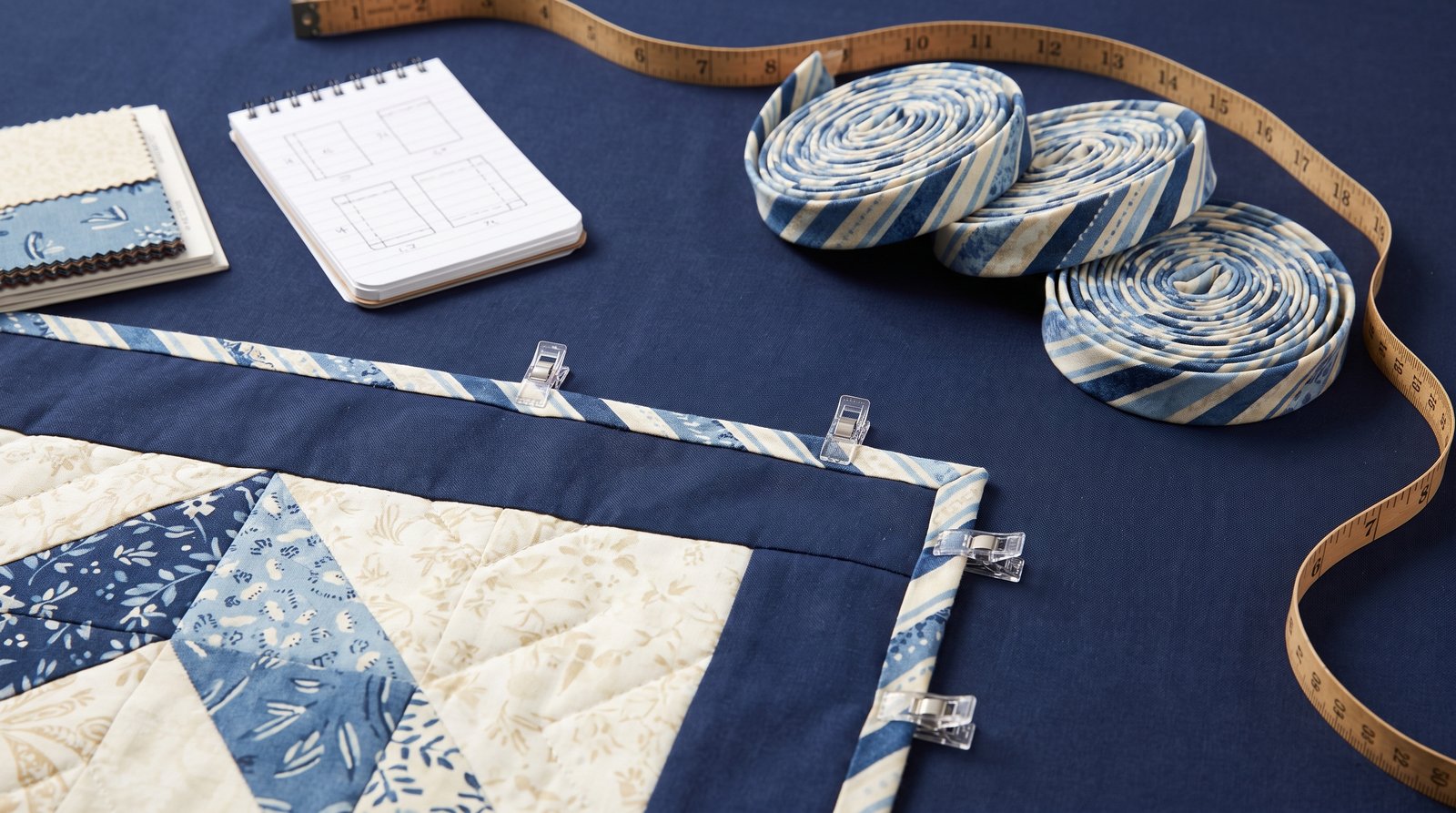 Binding strips, rotary cutter and quilting ruler laid out on a navy work surface